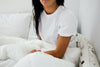 Woman with dark hair sitting in bed under a white blanket.